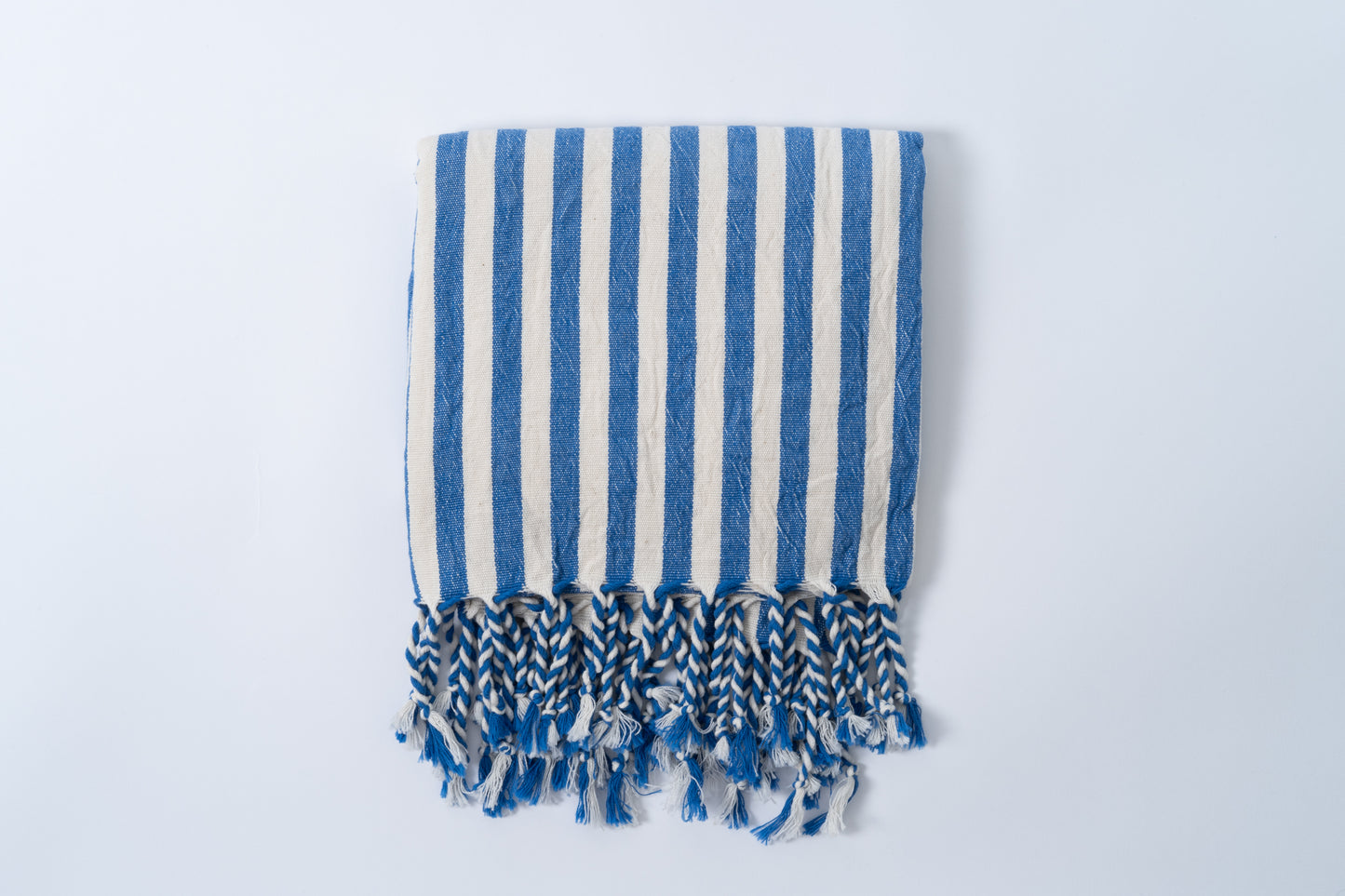 Blue and white striped towel with fringes on a light gray background