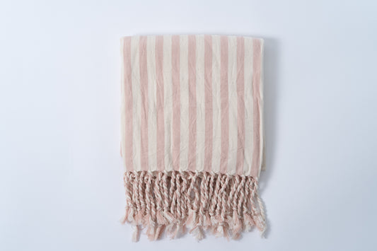 Striped pink and beige blanket with fringes on a light gray background