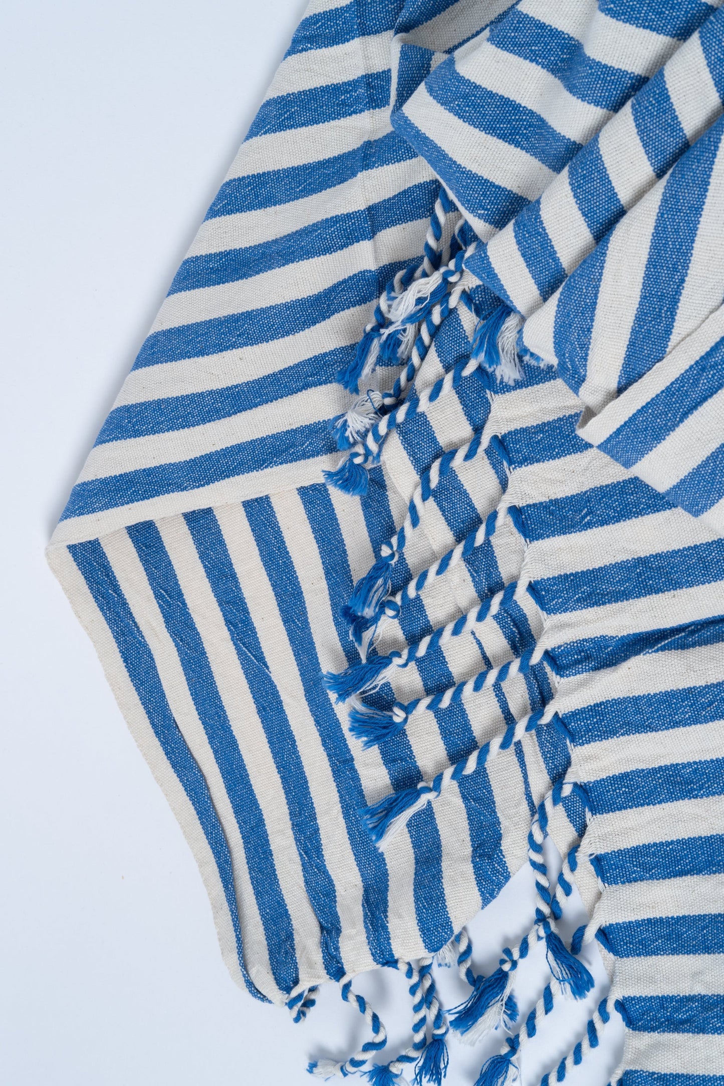 Blue and white striped towel with tassels on a light gray background