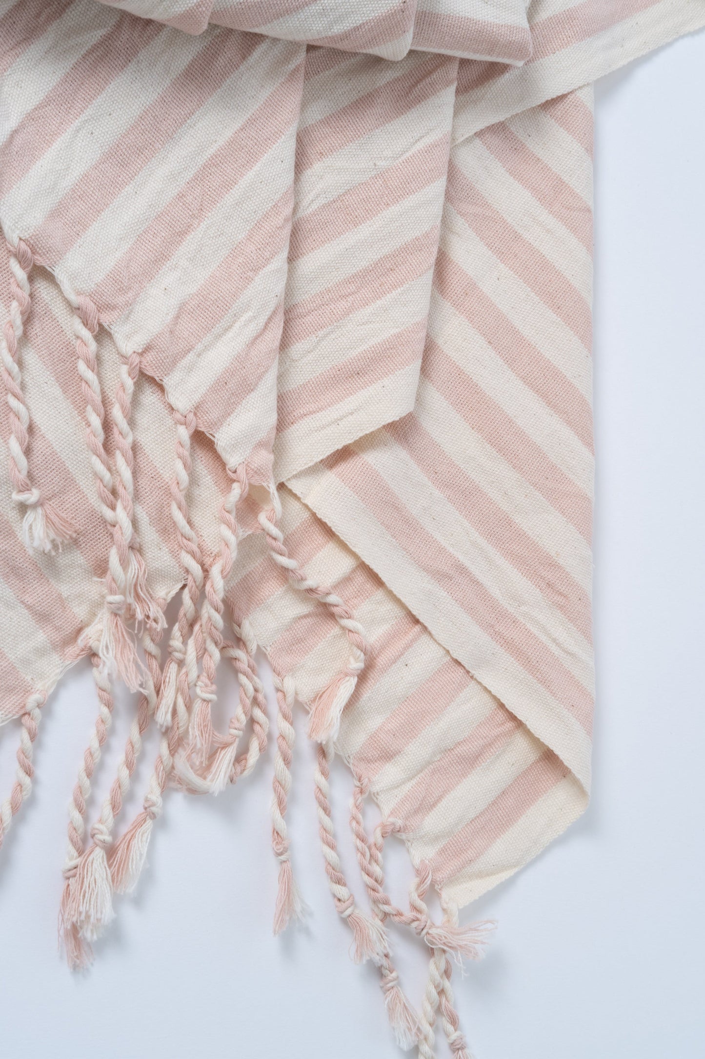 Pink and white striped towel with tassels on a light gray background