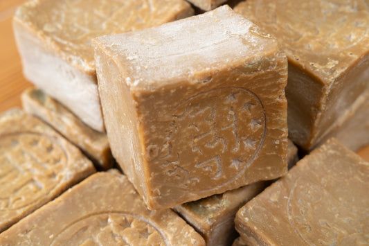 A stack of beige Aleppo soap bars with visible exfoliants, placed on a wooden surface.