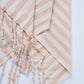 Pink and white striped towel with tassels on a light gray background