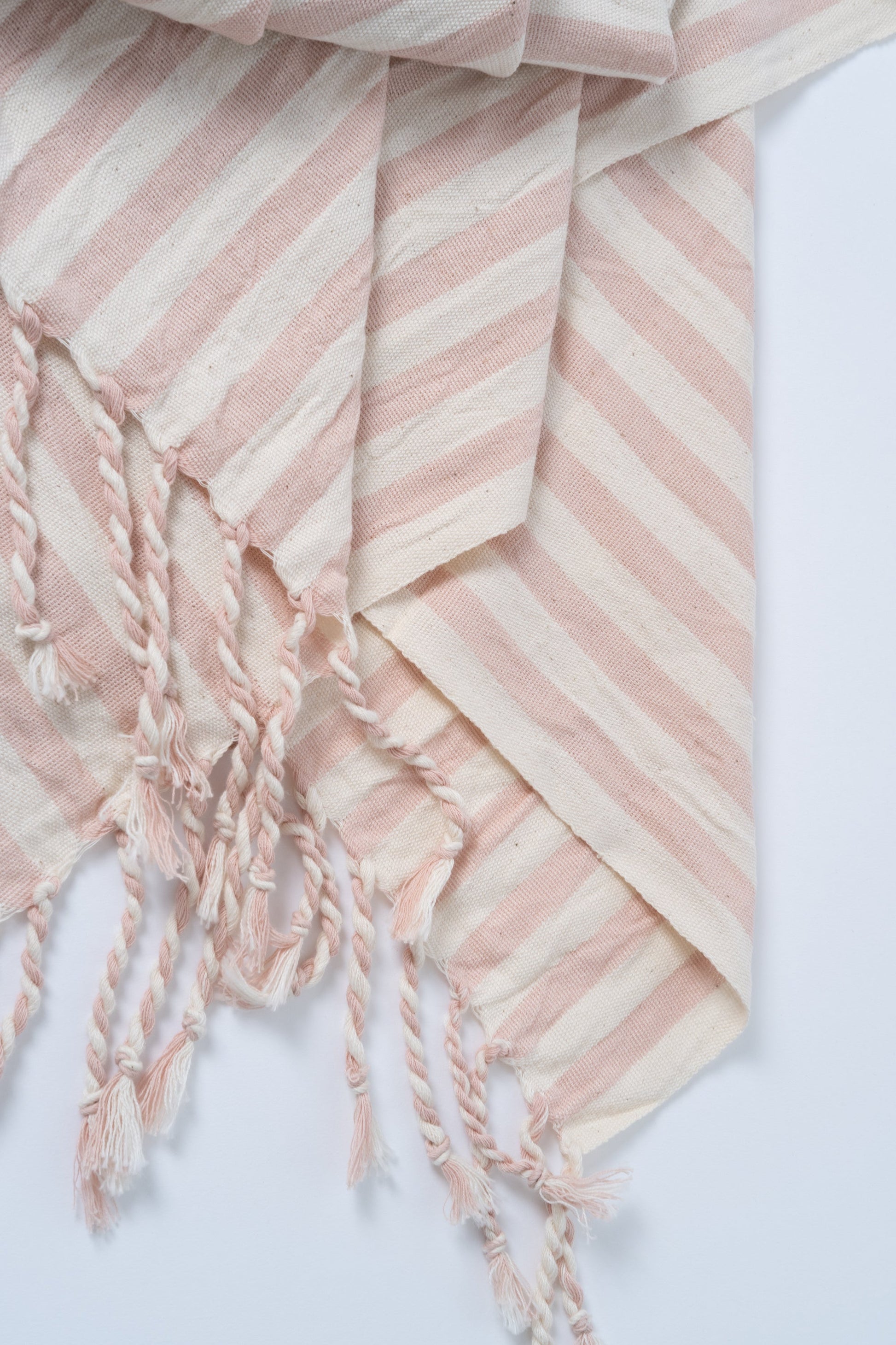 Pink and white striped towel with tassels on a light gray background